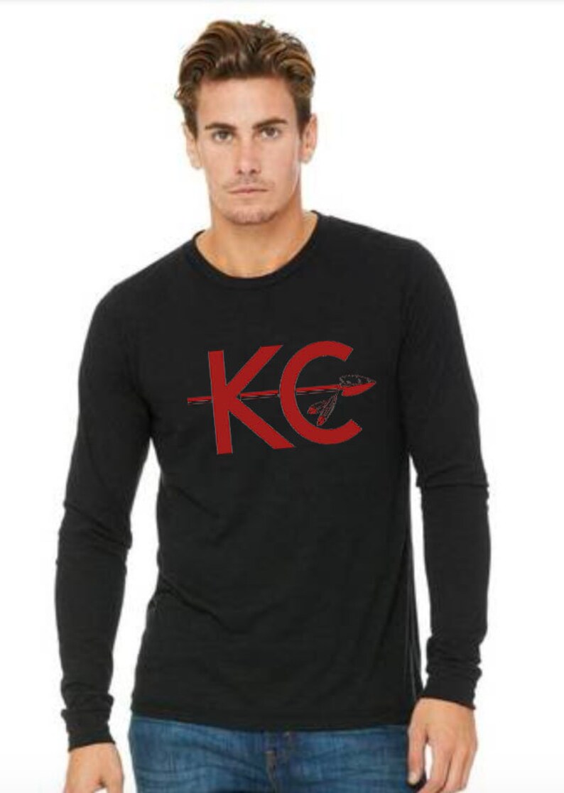 May include: Black long-sleeve shirt with a red graphic of the letters "KC" with an arrow through the "C".