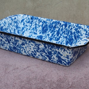 Puede incluir: Un molde para pan de color azul y blanco moteado con un borde negro. El molde está hecho de esmalte y tiene un aspecto vintage.