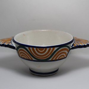 May include: A white ceramic bowl with two handles. The bowl has a blue, green, and orange geometric pattern around the rim.