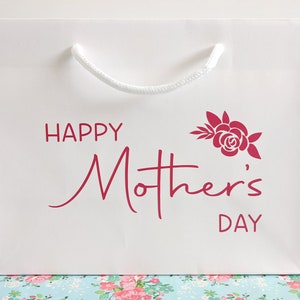 White gift bag with a rope handle. The bag has pink text that says "Happy Mother's Day" with a stylised rose and leaves.