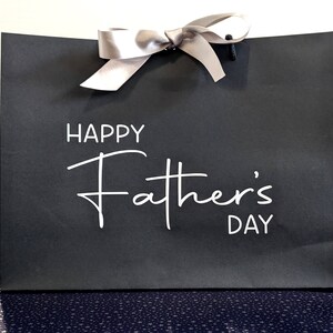 Black gift bag with a silver ribbon and the text "Happy Father's Day" in white.