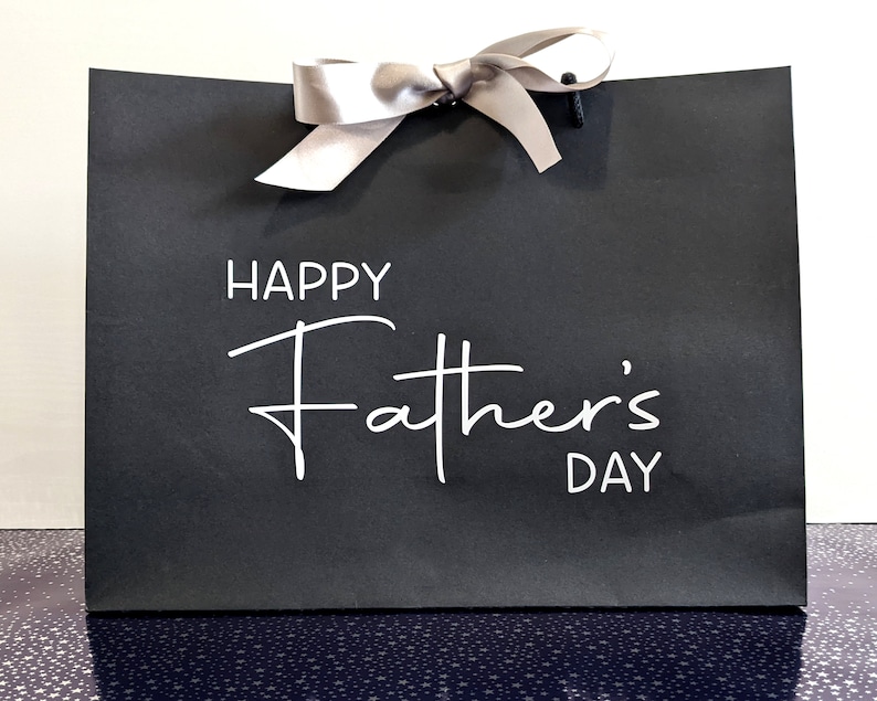 Black gift bag with a silver ribbon and the text "Happy Father's Day" in white.