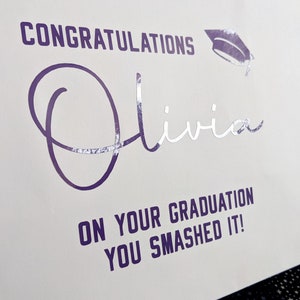 A white gift bag with purple text that reads "Congratulations Olivia on your graduation you smashed it!" with a purple graduation cap icon.