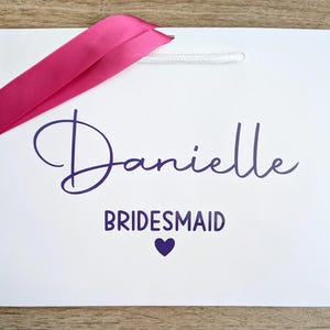 Personalised gift bag for a bridesmaid. The bag is white with purple text and a pink ribbon.