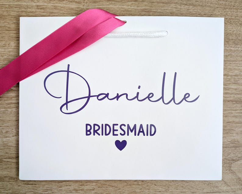 Personalised gift bag for a bridesmaid. The bag is white with purple text and a pink ribbon.