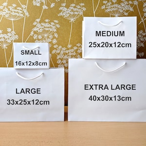 Four white paper gift bags with handles. The bags are labelled with the sizes: Small 16x12x8cm, Large 33x25x12cm, Medium 25x20x12cm, and Extra Large 40x30x13cm.