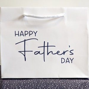 White gift bag with a blue inscription that reads "Happy Father's Day".