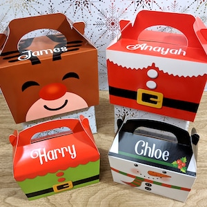 May include: Four Christmas-themed gift boxes with handles. The boxes are decorated with a reindeer, Santa Claus, an elf, and a snowman. Each box has a name on it: James, Anayah, Harry, and Chloe.