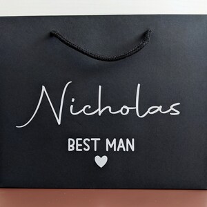 Black gift bag with a rope handle and the text "Nicholas Best Man" in white lettering with a small white heart.