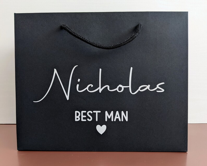 Black gift bag with a rope handle and the text "Nicholas Best Man" in white lettering with a small white heart.