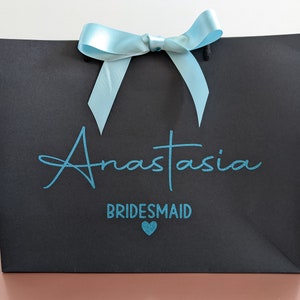 Black gift bag with a light blue bow and the text "Anastasia Bridesmaid" in teal blue lettering with a small teal heart.
