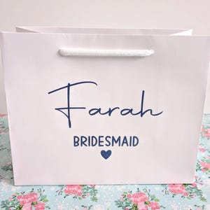White gift bag with a blue inscription that reads "Farah Bridesmaid" with a small blue heart.