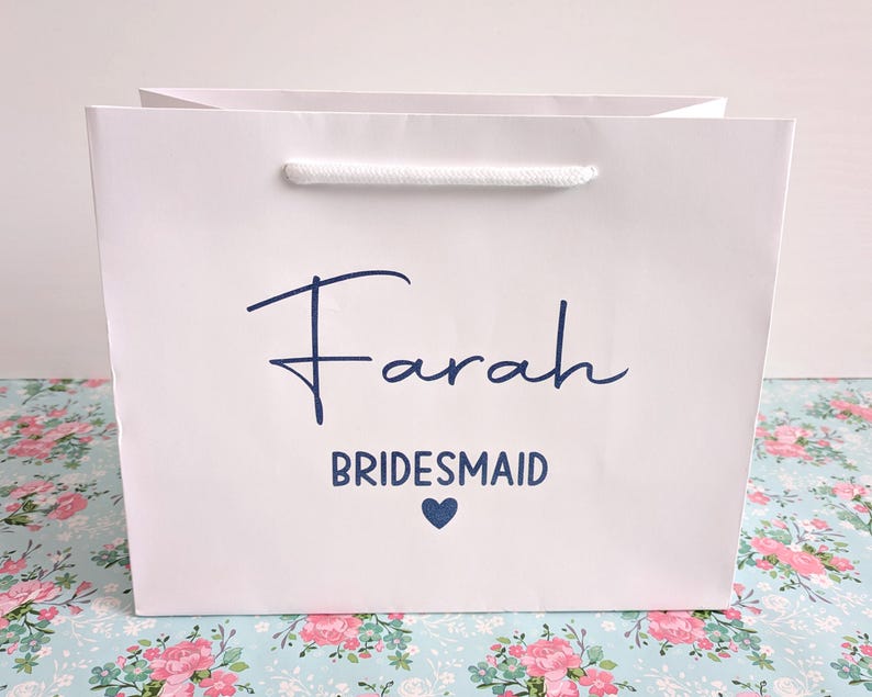 White gift bag with a blue inscription that reads "Farah Bridesmaid" with a small blue heart.