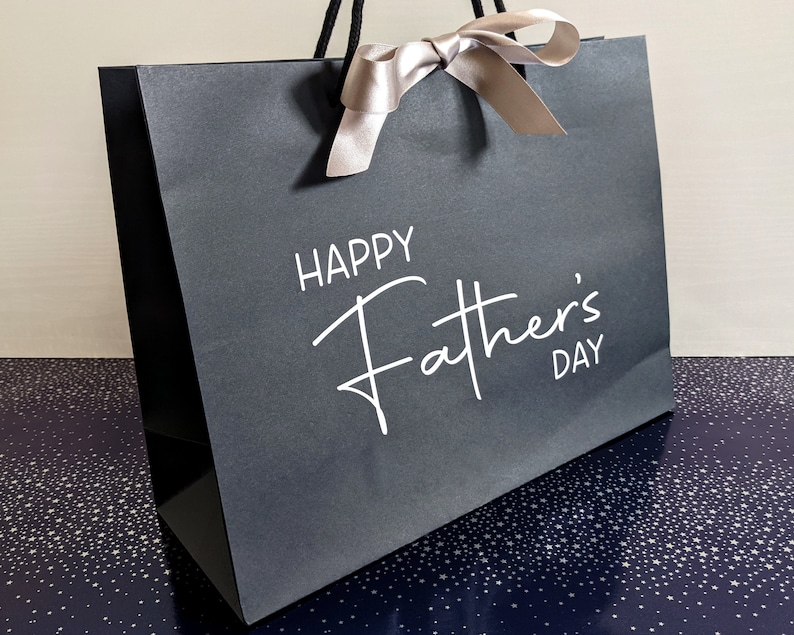 A black gift bag with a white satin ribbon and the text "Happy Father's Day" printed on the front.