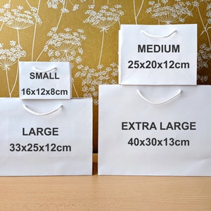 Four white paper gift bags with handles. The bags are labelled with the sizes: Small 16x12x8cm, Large 33x25x12cm, Medium 25x20x12cm, and Extra Large 40x30x13cm.