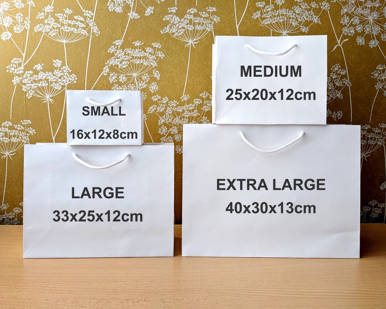 Four white paper gift bags with handles. The bags are labelled with the sizes: Small 16x12x8cm, Large 33x25x12cm, Medium 25x20x12cm, and Extra Large 40x30x13cm.