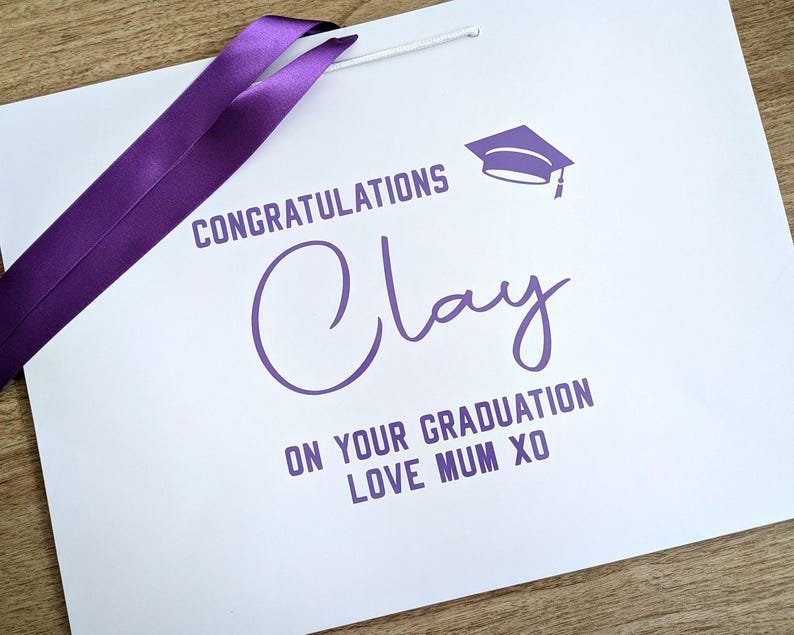 White graduation gift bag with purple text and satin ribbon.