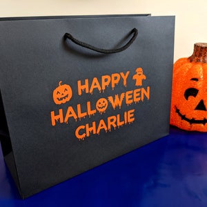 Black gift bag with orange text that says "Happy Halloween Charlie" with a pumpkin and ghost graphic.