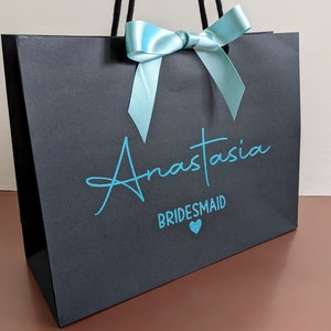 Black bridesmaid gift bag with a blue bow and the text "Anastasia Bridesmaid" in blue lettering.