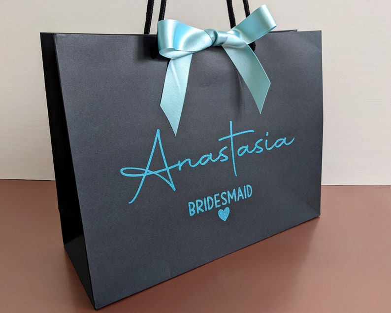 Black bridesmaid gift bag with a blue bow and the text "Anastasia Bridesmaid" in blue lettering.