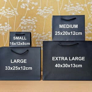 Four black gift bags of different sizes. The bags are labelled with the size and dimensions in centimetres: Small 16x12x8cm, Large 33x25x12cm, Medium 25x20x12cm, Extra Large 40x30x13cm.