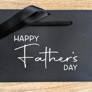Black gift bag with Happy Father's Day in white text, and a black ribbon.