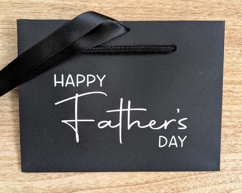 Black gift bag with Happy Father's Day in white text, and a black ribbon.