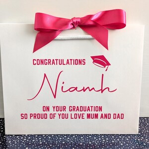 A small white gift bag with pink text and ribbon with a Congratulations on your Graduation message.