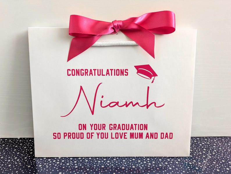 A small white gift bag with pink text and ribbon with a Congratulations on your Graduation message.