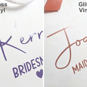 Two gift bags with personalised names, one with purple glossy vinyl, and the other with rose gold glitter vinyl.