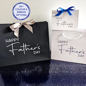 A selection of Father's Day gift bags in black and white. They have the text "Happy Father's Day" on the bags in different colours. Two of the bags have satin ribbon.