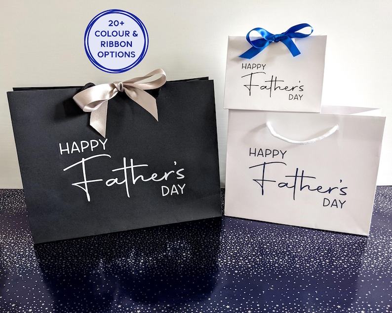 A selection of Father's Day gift bags in black and white. They have the text "Happy Father's Day" on the bags in different colours. Two of the bags have satin ribbon.