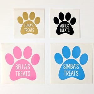 May include: Four square stickers featuring paw print designs in gold, black, pink, and blue. Each paw print has a name and the word "Treats" in white text: Luna's, Alfie's, Bella's, and Simba's. Ideal for pet owners.