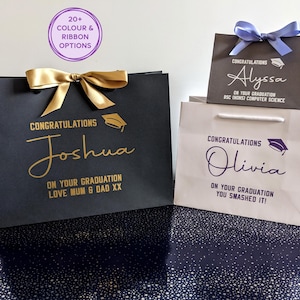 Personalised graduation gift bags in black, white and grey with ribbon. Bags say Congratulations on your graduation, with a mortar board motif, the graduate's name in large cursive text, and then a personalised message in smaller text is below.