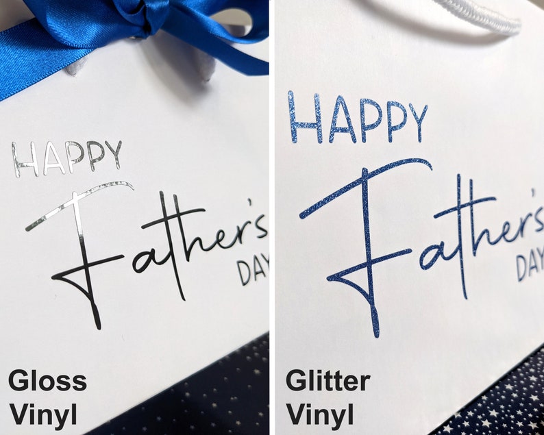 Two gift bags with the text "Happy Father's Day" printed on them. The bag on the left has the text in black gloss vinyl. The bag on the right has the text in blue glitter vinyl.