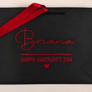 Black medium gift bag with red text and satin ribbon. It reads "Briana Happy Valentine's Day".