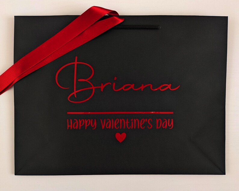 Black medium gift bag with red text and satin ribbon. It reads "Briana Happy Valentine's Day".