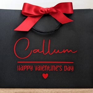 Black gift bag with a red bow and the text "Callum Happy Valentine's Day" in red lettering.