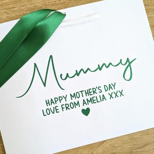 White gift bag with green ribbon and text which reads "Mummy Happy Mother's Day Love from Amelia xxx"