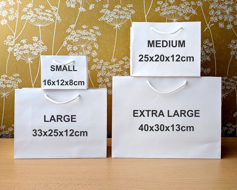 Four white paper gift bags with handles. The bags are labelled with the sizes: Small 16x12x8cm, Large 33x25x12cm, Medium 25x20x12cm, and Extra Large 40x30x13cm.
