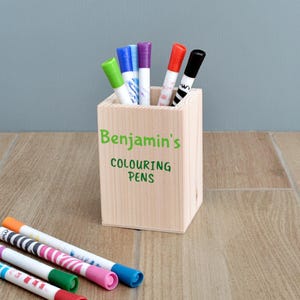 May include: A wooden pencil holder with the words "Benjamin's Colouring Pens" written on it. The holder is filled with colourful markers.