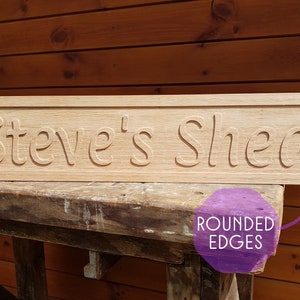 May include: A wooden sign with rounded edges that reads "Steve's Shed". The sign is made of light brown wood and has a natural finish.
