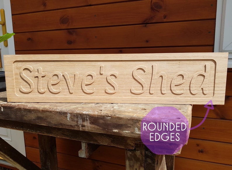 May include: A wooden sign with rounded edges that reads "Steve's Shed". The sign is made of light brown wood and has a natural finish.