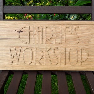 May include: A wooden sign with the text "Charlie's Workshop" carved into it. The sign is light brown and has a slightly rough texture.