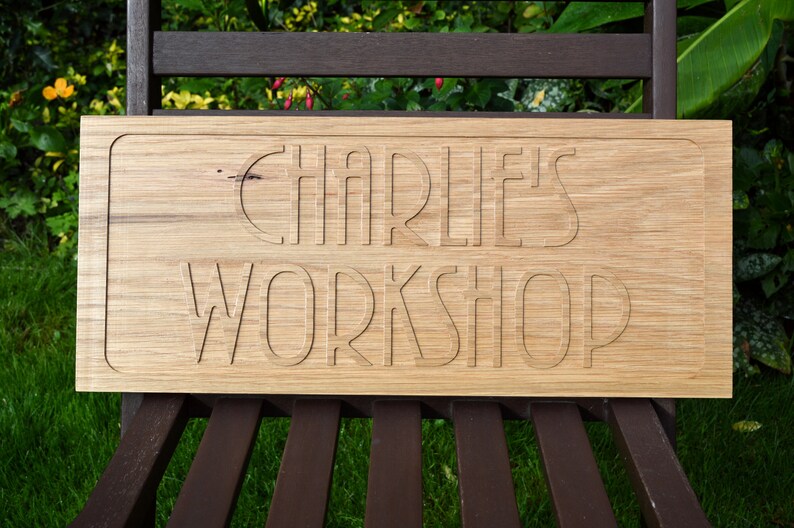 May include: A wooden sign with the text "Charlie's Workshop" carved into it. The sign is light brown and has a slightly rough texture.