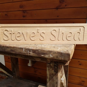 May include: A wooden sign with the text "Steve's Shed" carved into it. The sign is light brown and has a slightly weathered look.