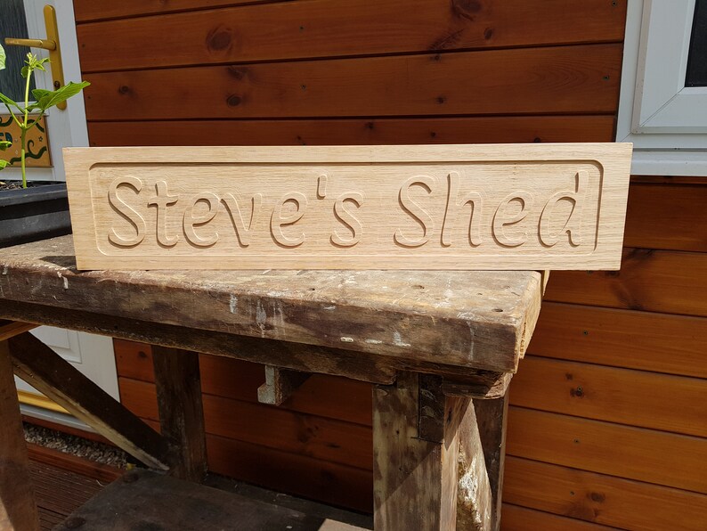May include: A wooden sign with the text "Steve's Shed" carved into it. The sign is light brown and has a slightly weathered look.
