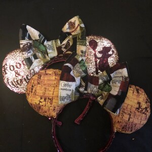 Puede incluir: Diadema burdeos con orejas en forma de corcho y un lazo con etiquetas de botellas de vino. Una oreja tiene el texto "Food & Wine". Las orejas están decoradas con lentejuelas.