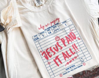Könnte beinhalten: Cremefarbenes T-Shirt mit den roten Aufschriften "why we paying" und "JESUS PAID IT ALL!!". Das Design ähnelt einer Rechnung, mit zusätzlichem Text wie "ALL THESE BILLS WHEN", "Jesus" und "PAID IN FULL".