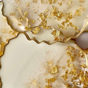 May include: Two white resin coasters with a wavy edge and gold leaf accents.